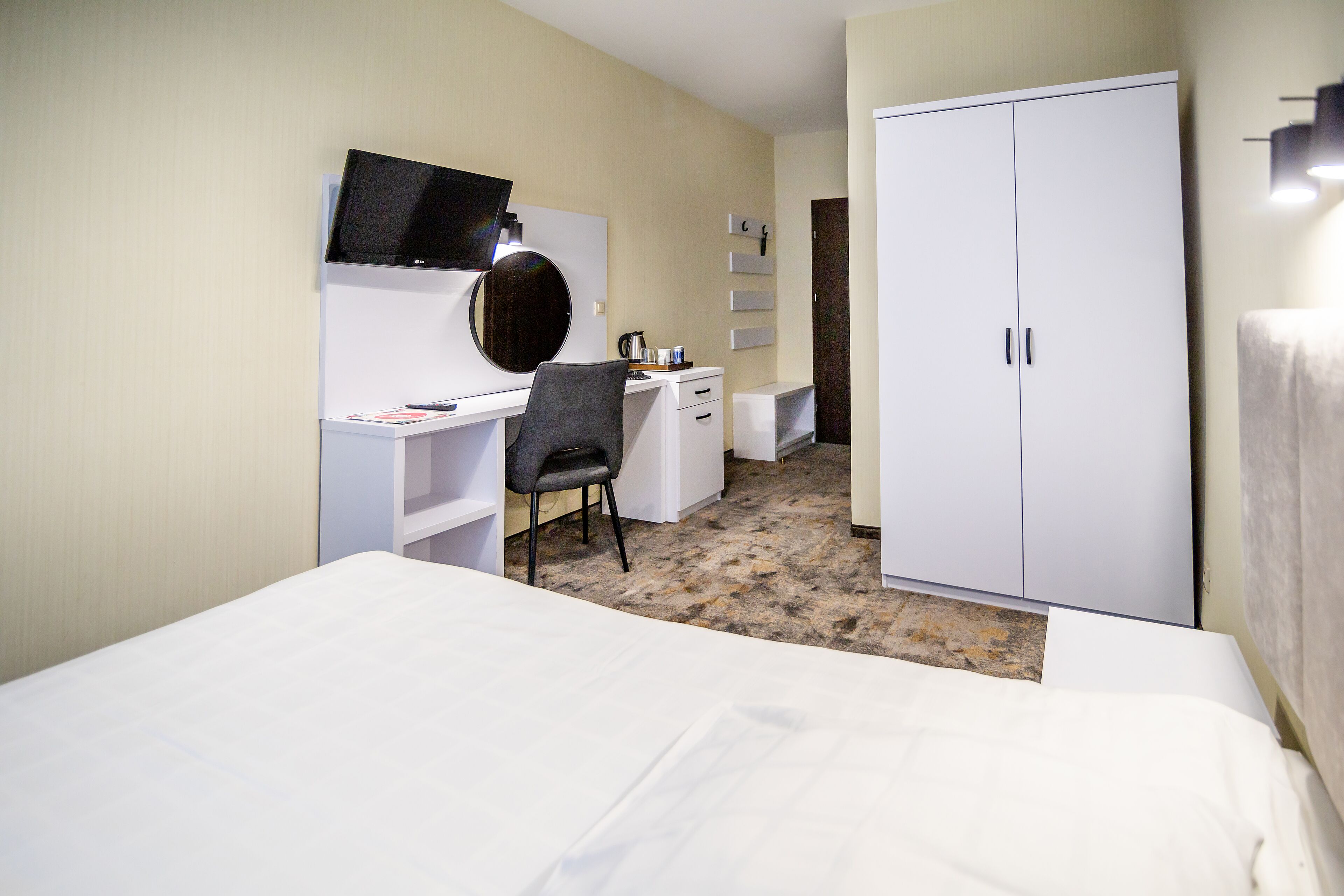 Habitación de hotel con cama, escritorio con silla, televisor, armario y una mesita con hervidor.