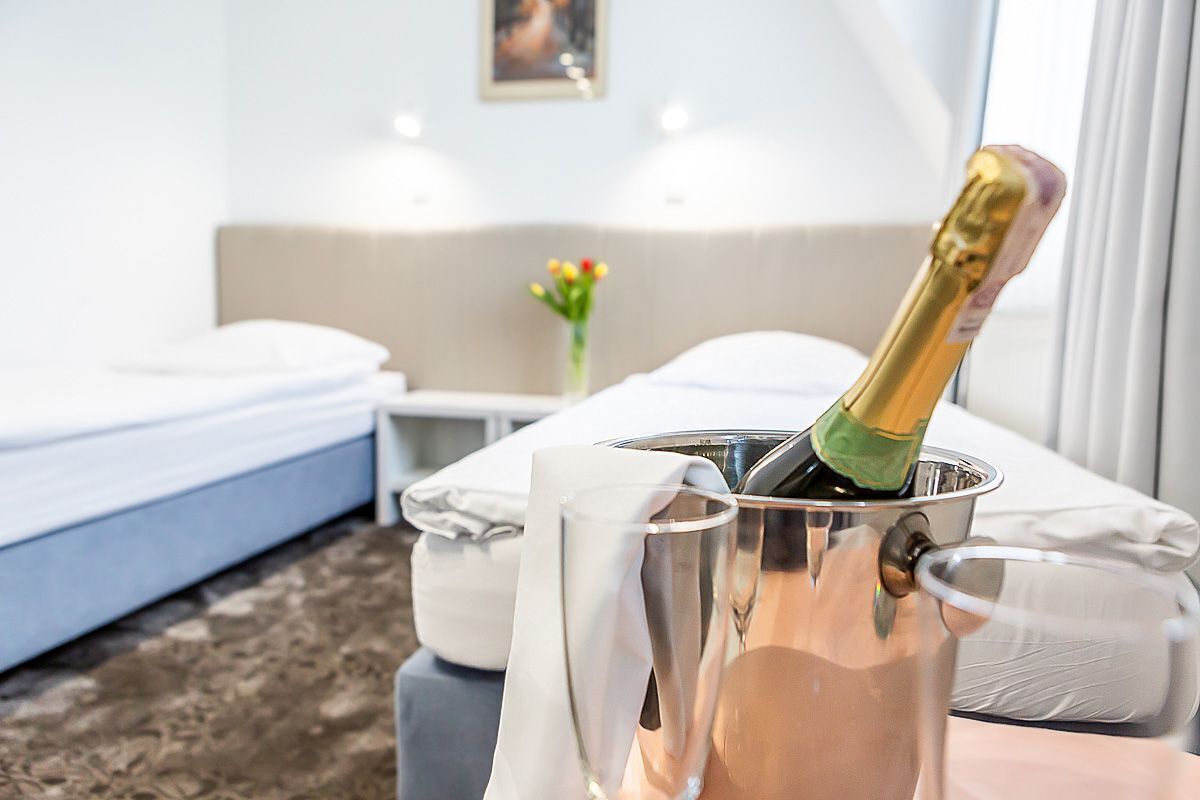 Een hotelkamer met een bed, een klein tafeltje met een champagnefles en een vaas met bloemen.