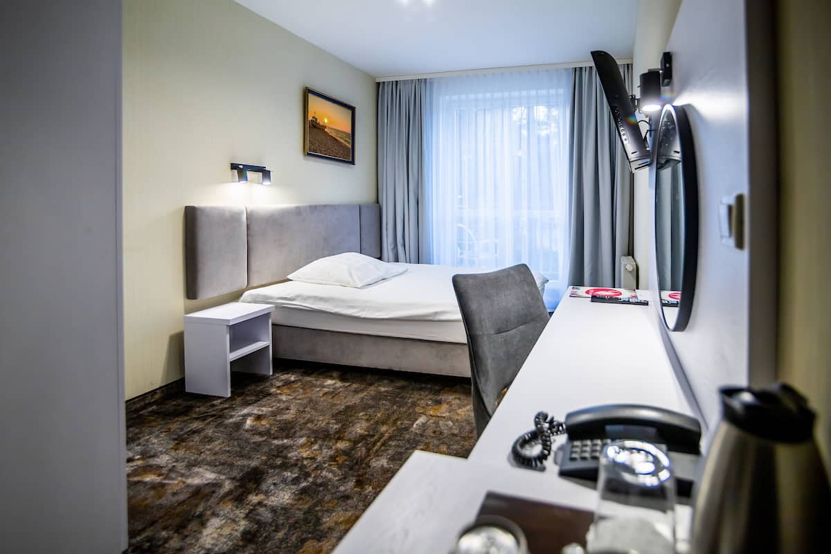 Une chambre d’hôtel comprenant un lit, une table de chevet, un bureau avec un téléphone et une bouilloire, ainsi qu’une fenêtre avec des rideaux.