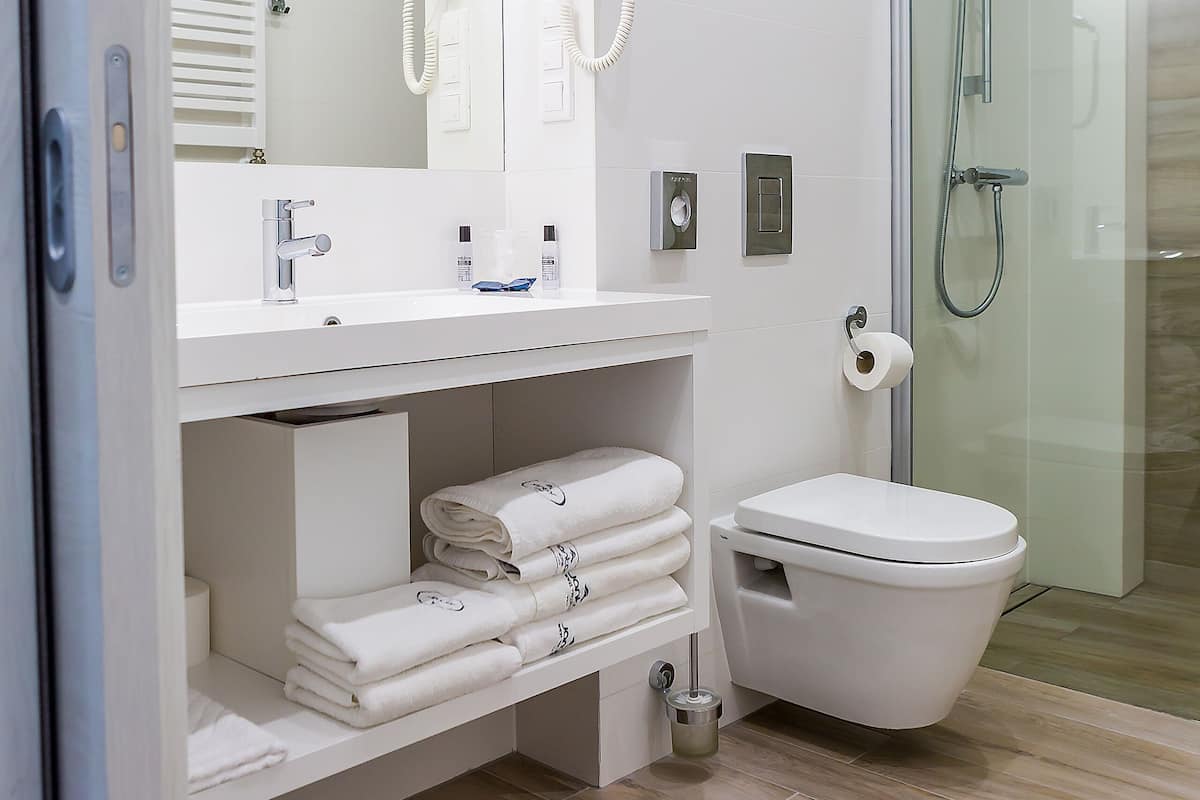 Une salle de bain moderne avec une douche à parois de verre, un lavabo blanc avec un miroir et des serviettes soigneusement pliées sur une étagère.