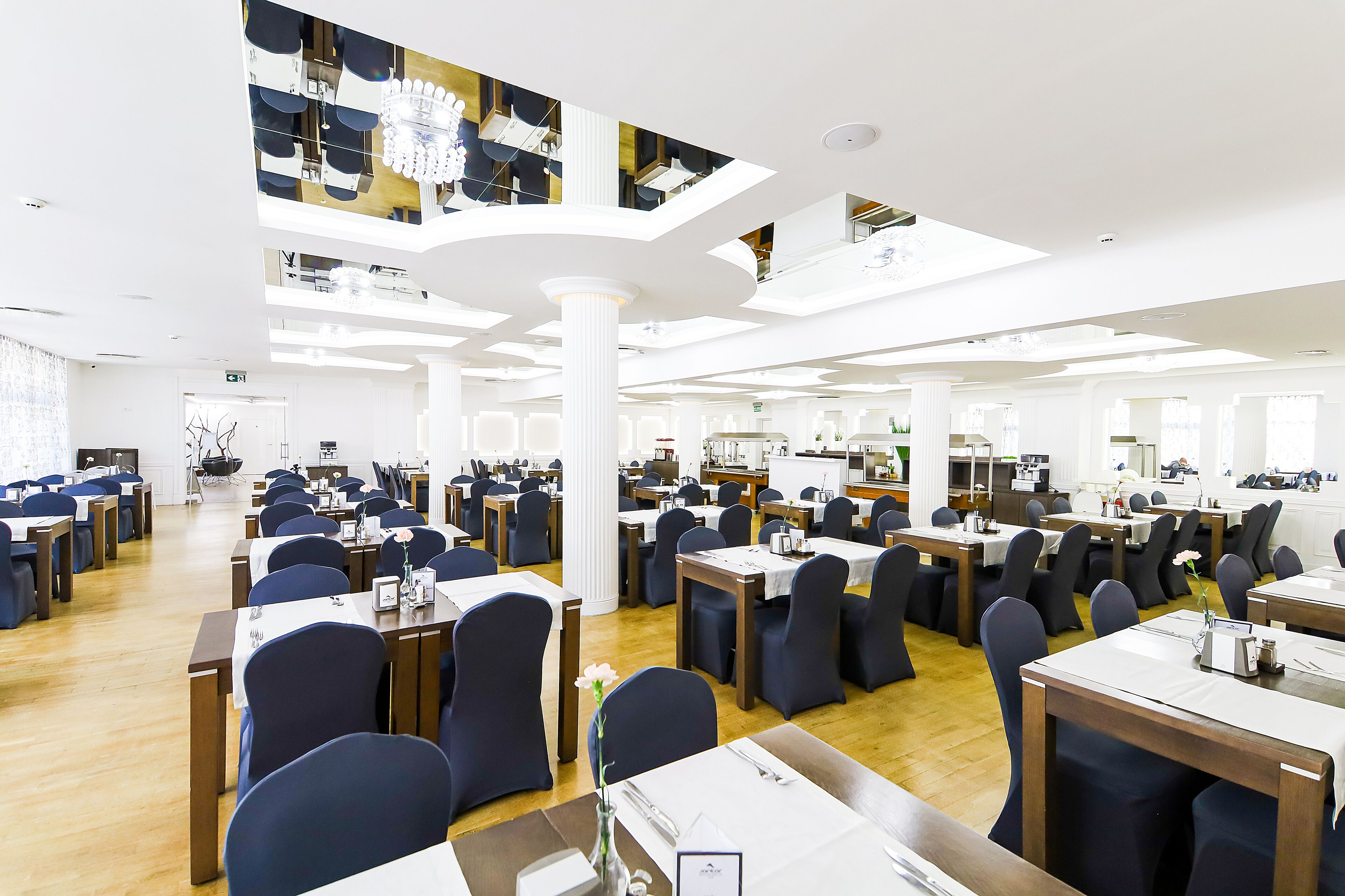 Un vaste espace dédié à la salle à manger, avec de nombreuses tables et chaises, de hauts plafonds dotés de puits de lumière et une colonne centrale.