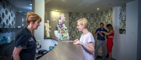 A reception area with a reception desk, a decorative orchid arrangement, and a statue on the wall.