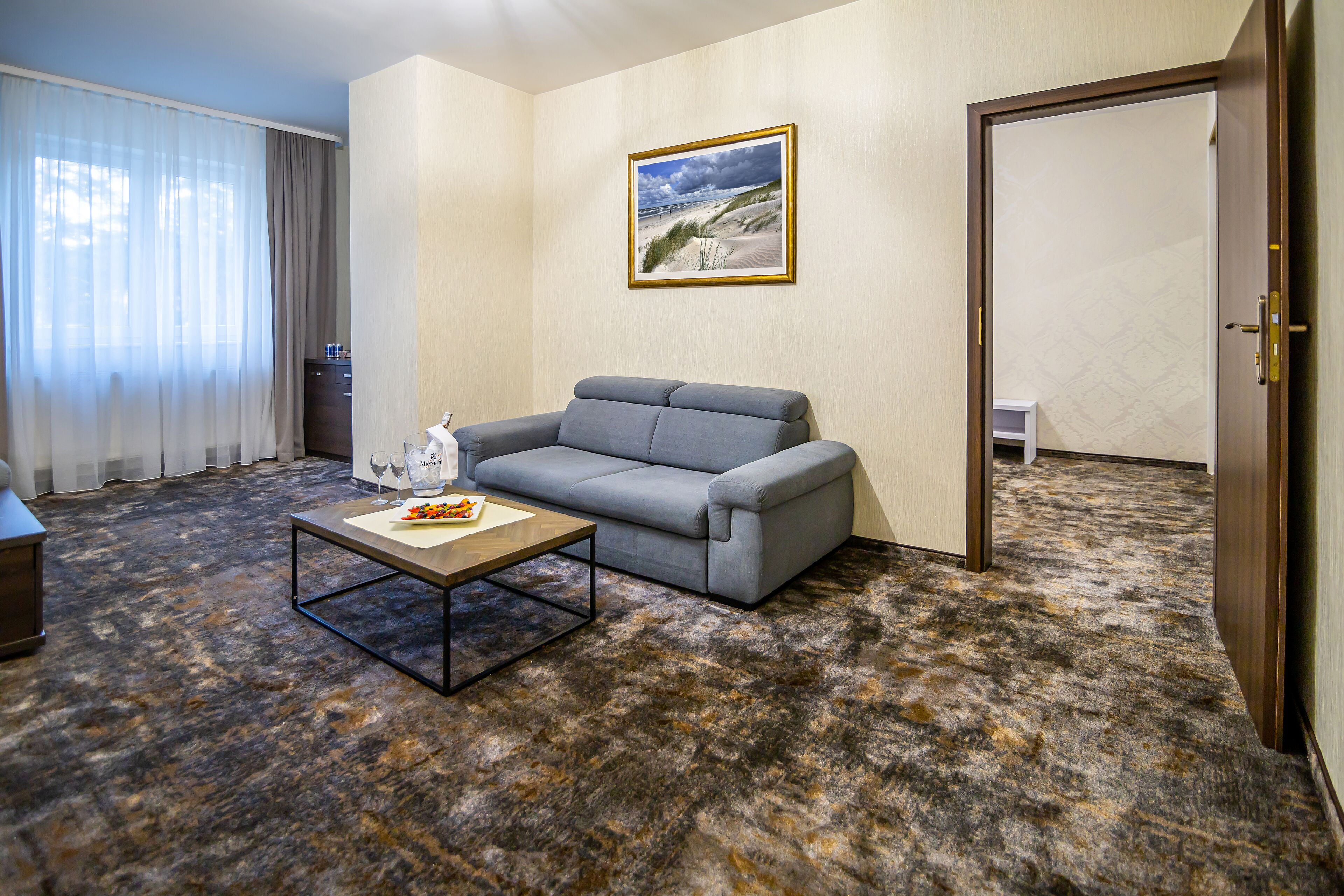 A room with a gray sofa, a coffee table, and a painting of a beach scene.