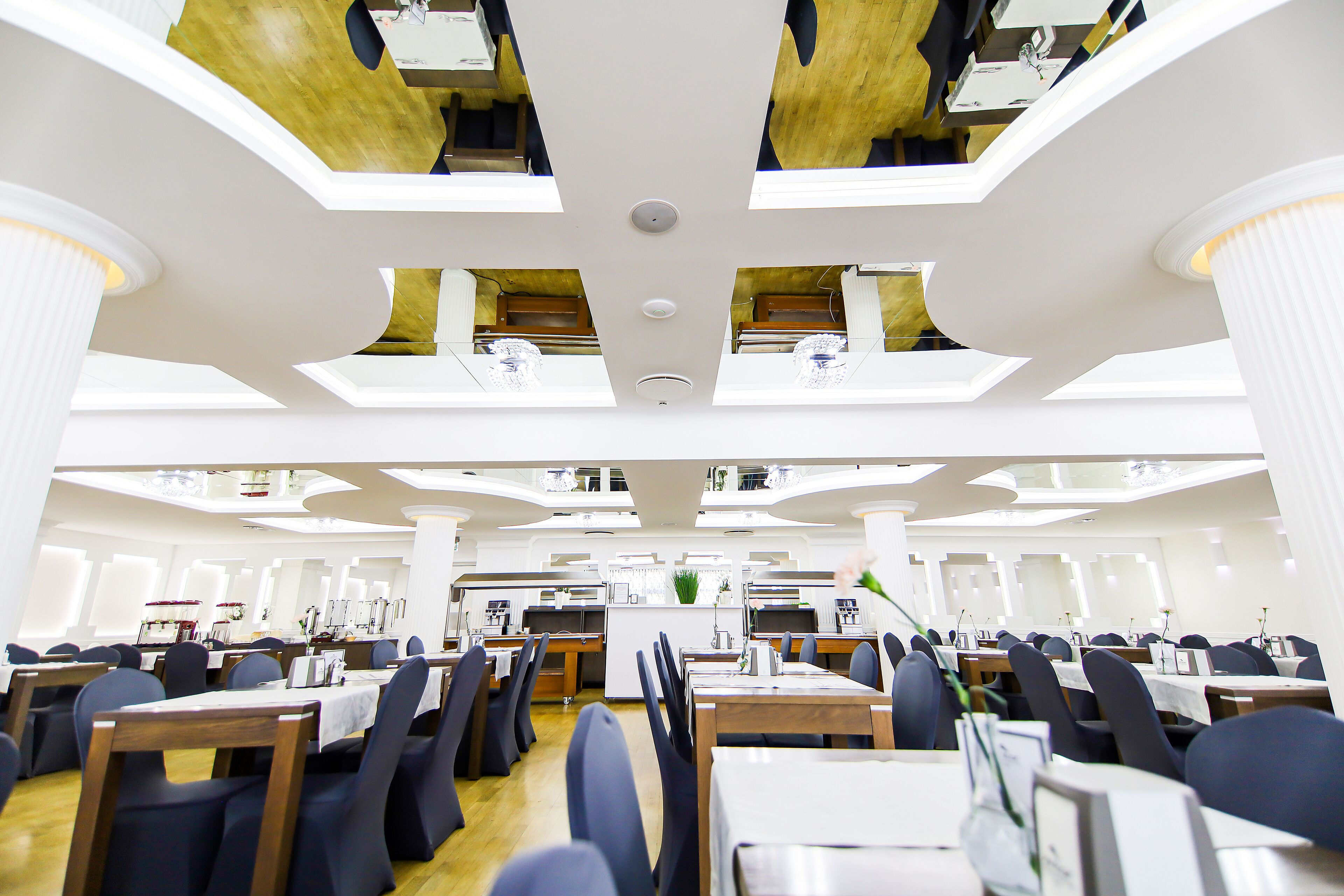 A spacious dining area with multiple tables and chairs, a central service counter, and a high ceiling with recessed lighting.