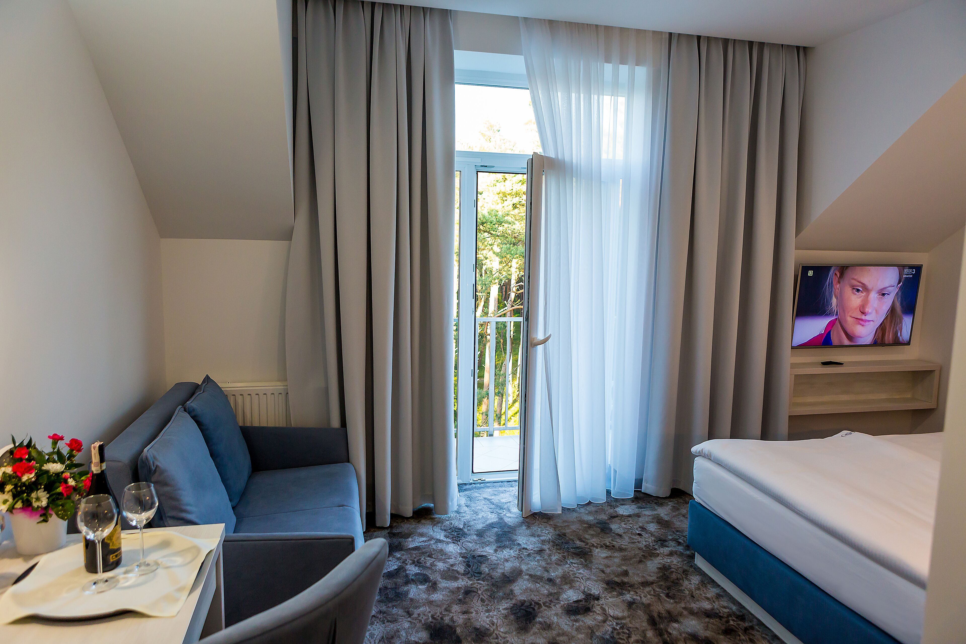 Een hotelkamer met een bank, een bed, een televisie, een tafel met een fles en glazen, en uitzicht op het omliggende landschap.