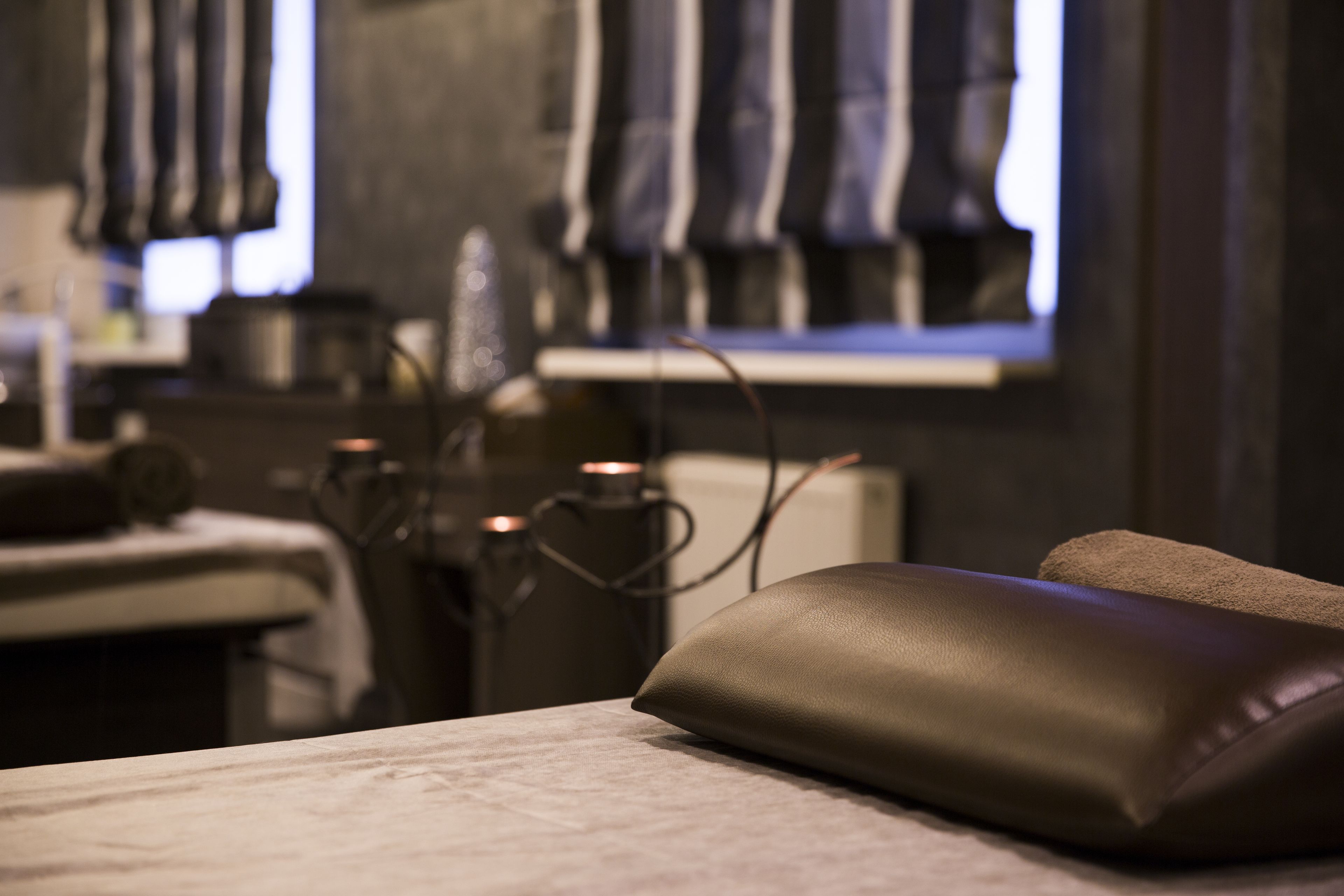 A massage chair in a spa room with a window and a towel rack in the background.