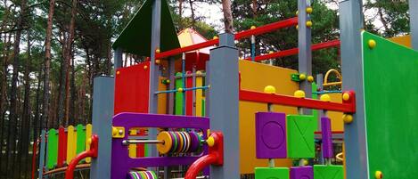 Ein Spielplatz mit verschiedenen Klettergerüsten und Rutschen, umgeben von Bäumen.