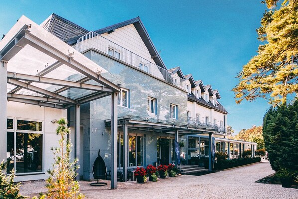 A modern hotel with a covered outdoor area, large windows, and a well-maintained garden. - Hotel Jantar (Ustka)