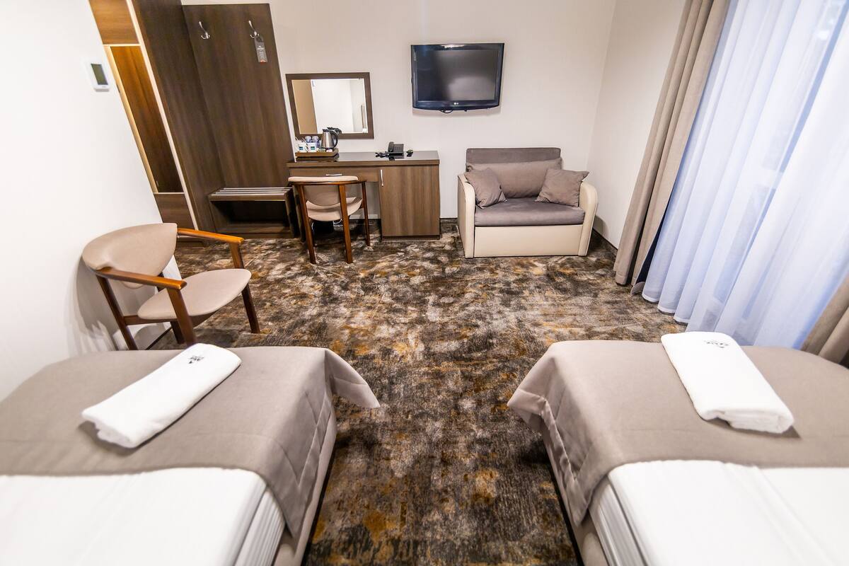 Une chambre d’hôtel avec deux lits, un bureau, une chaise, une télévision et une grande fenêtre avec des rideaux.