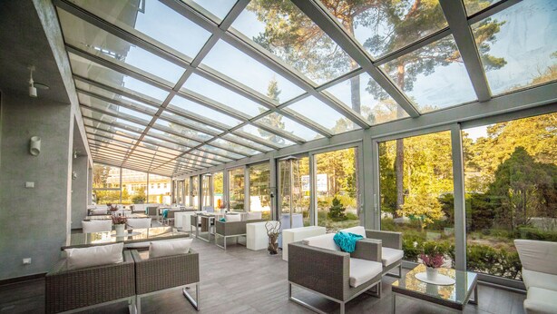 A spacious glass-enclosed lounge area with modern furniture and a view of the surrounding trees. - Hotel Jantar (Ustka)
