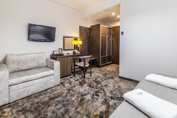 Une chambre d’hôtel avec un canapé, un bureau avec une lampe, une télévision et un dressing.