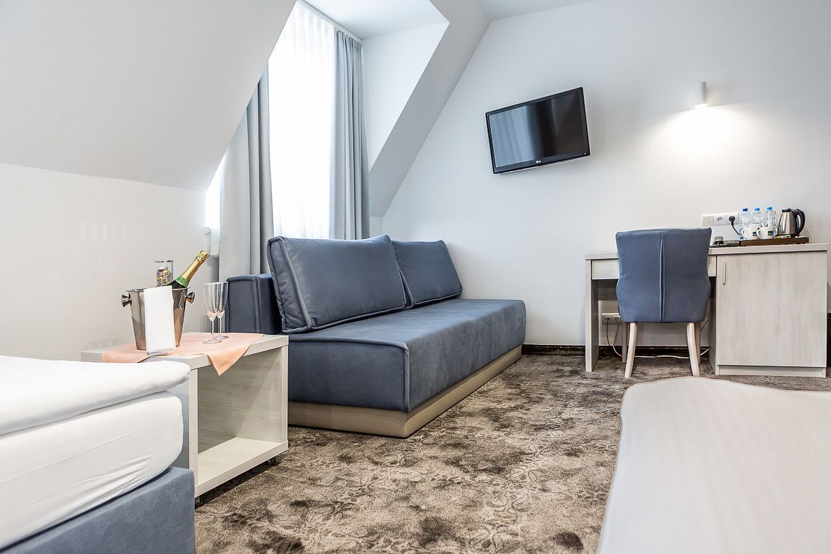 Moderni hotellihuone, jossa on vuodesohva, työpöytä tuolilla, taulutelevisio ja pieni keittonurkkaus.