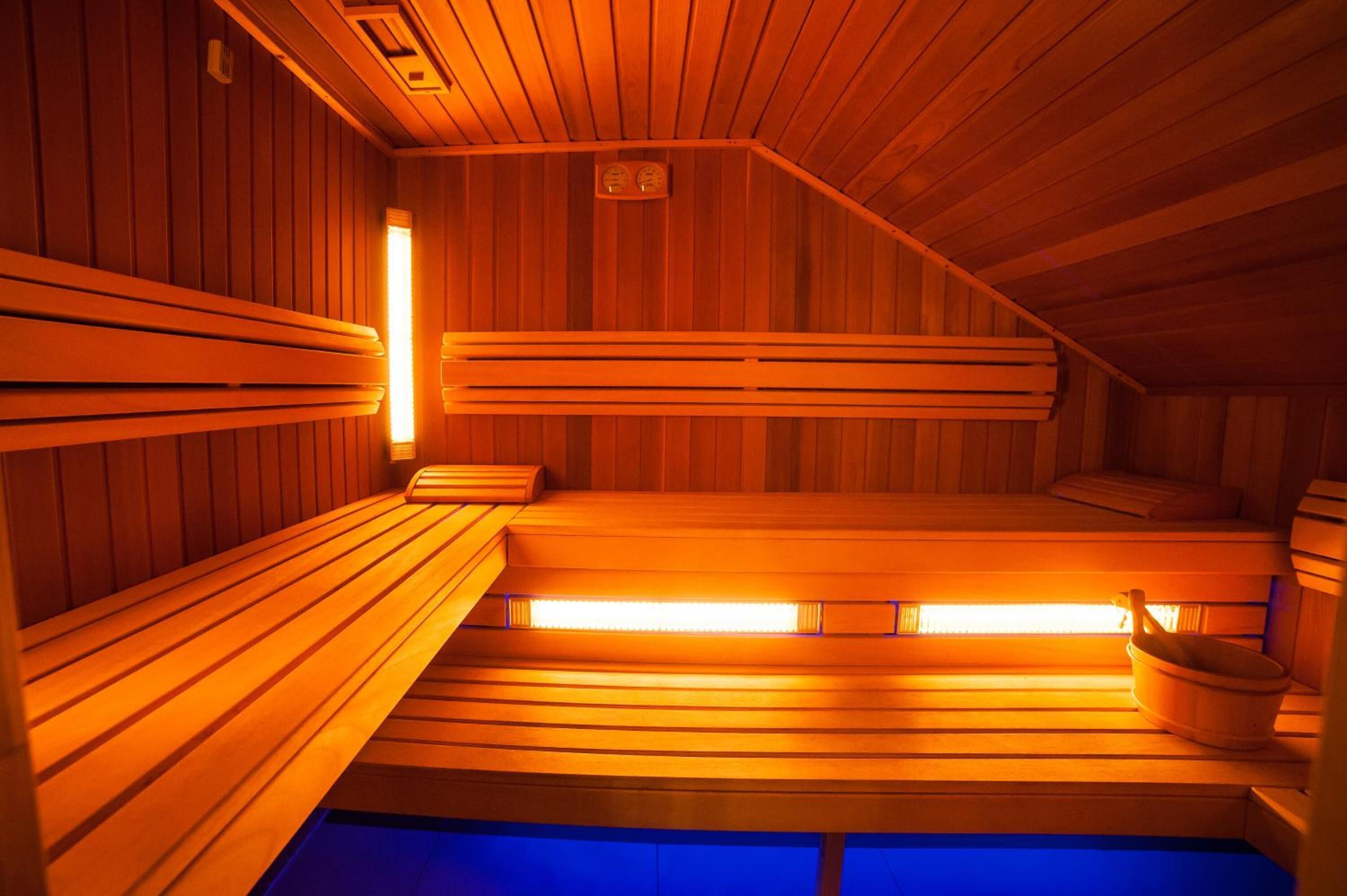 Un sauna avec des bancs en bois, un radiateur fixé au mur et un petit seau.