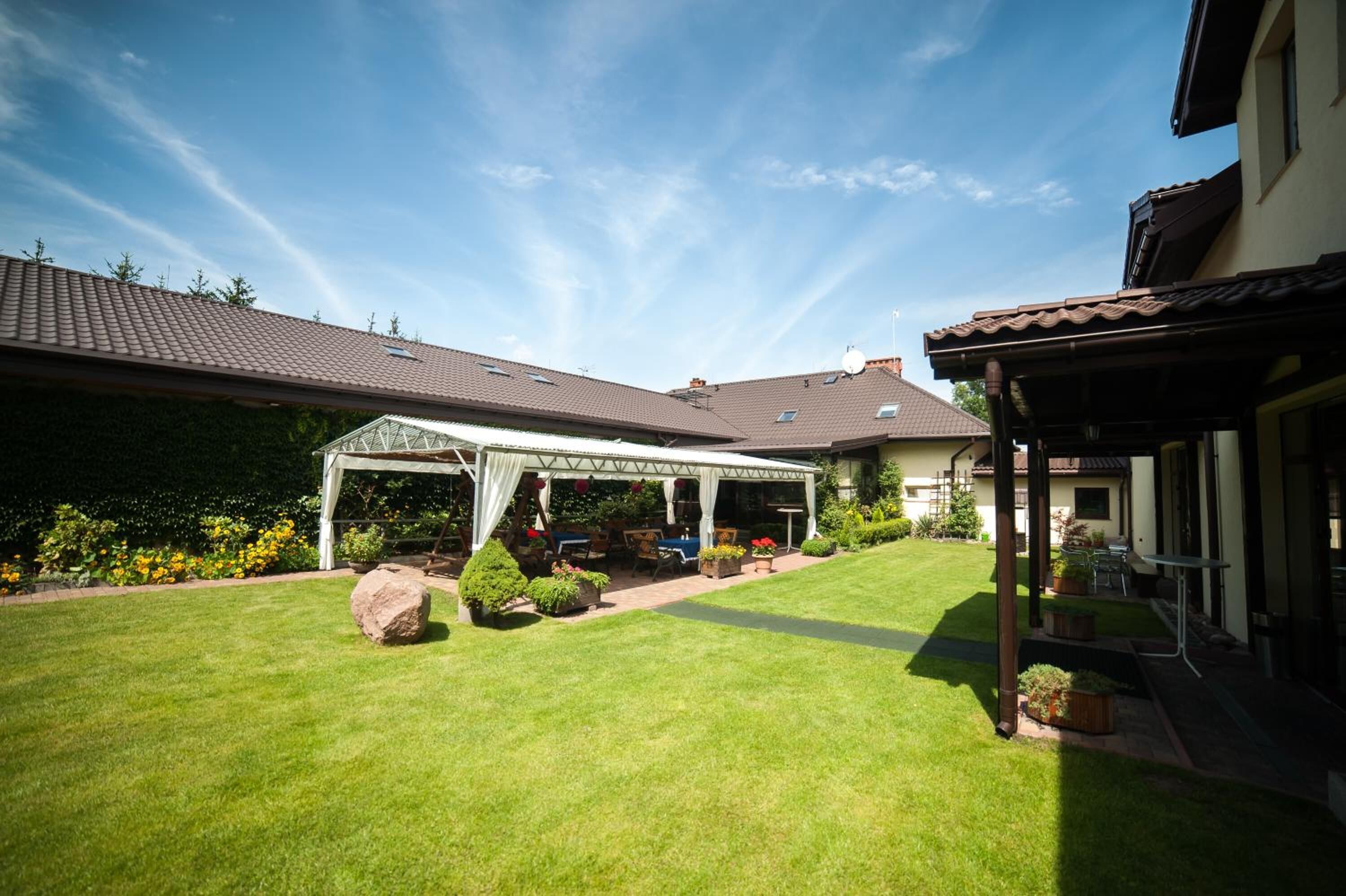 A well-maintained garden with a covered patio area, a lawn, and a house with a tiled roof.