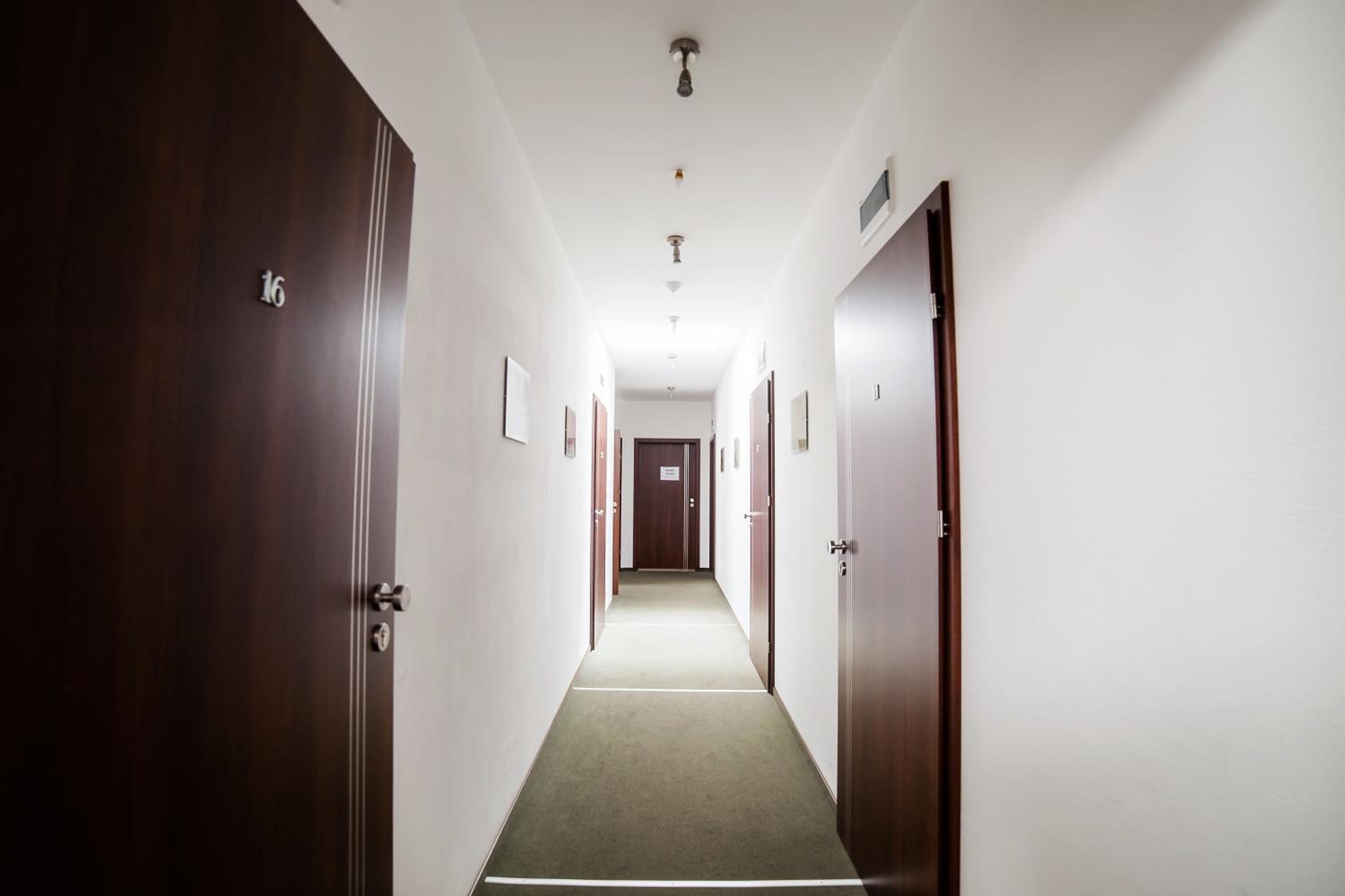 Un pasillo de hotel con puertas de madera, suelo alfombrado y una pared blanca con un número de puerta.