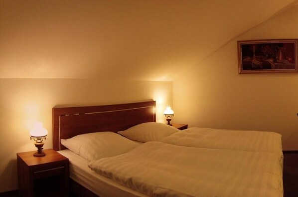 A single bed with a wooden headboard in a hotel room. There are two bedside lamps on either side of the bed.