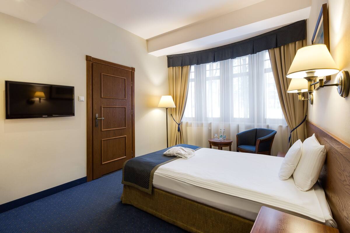 Une chambre d’hôtel comprenant un lit, un téléviseur fixé au mur, un bureau avec une chaise et une fenêtre avec des rideaux.