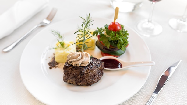 A plate with a steak, mashed potatoes, and a cherry tomato on a stick, accompanied by a glass of red wine.