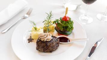 A plate with a steak, mashed potatoes, and a cherry tomato on a stick, accompanied by a glass of red wine.