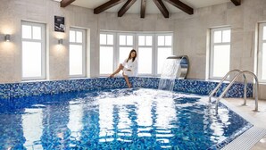A large indoor swimming pool with a mosaic tile border, a waterfall feature, and a person relaxing by the pool. - Bukowy Park Hotel Medical Spa (Polanica-Zdroj)