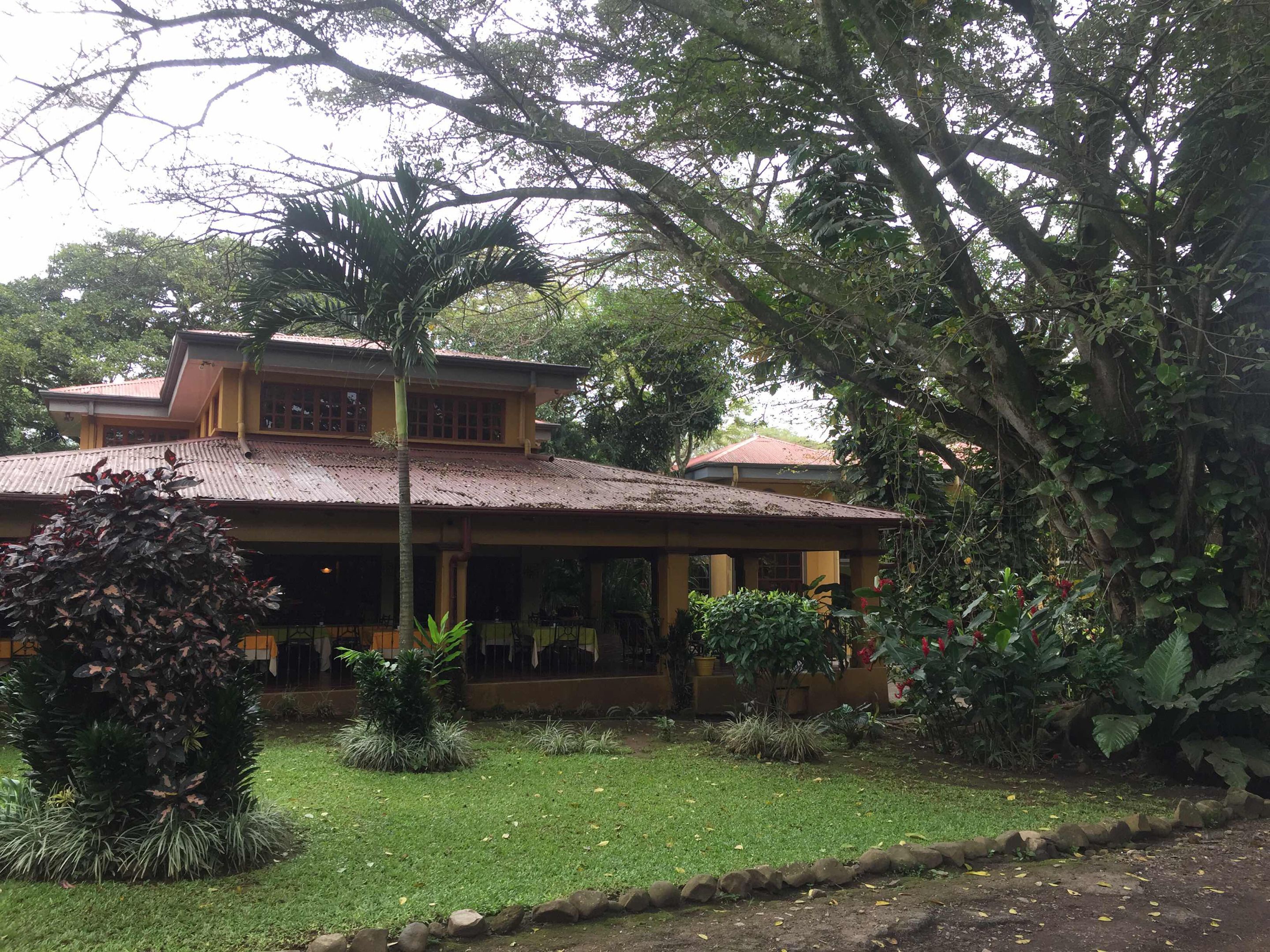 A two-story house with a tiled roof, surrounded by lush greenery and a well-maintained garden.