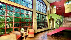 A spacious room with large windows, a staircase, and wicker furniture. - Trapp Family Country Inn (San Antonio)