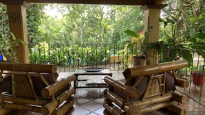 A covered outdoor seating area with bamboo furniture, surrounded by potted plants and a view of a lush garden. - Trapp Family Country Inn (San Antonio)