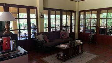 A living room with a sofa, coffee table, and a lamp. There are large windows with a view of the outside.