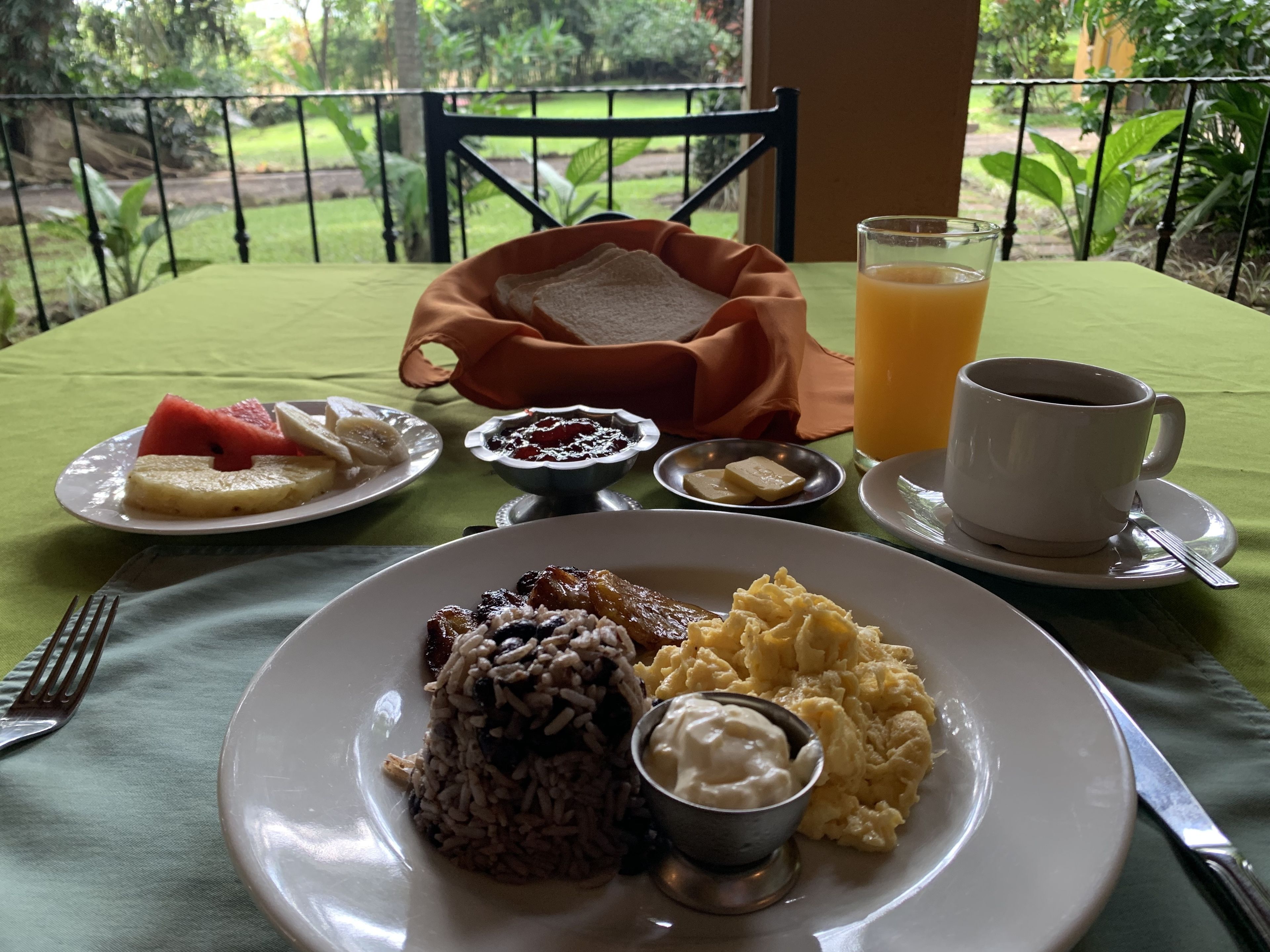 A breakfast setting with plates of food, a glass of orange juice, and a cup of coffee on a table with a green tablecloth.