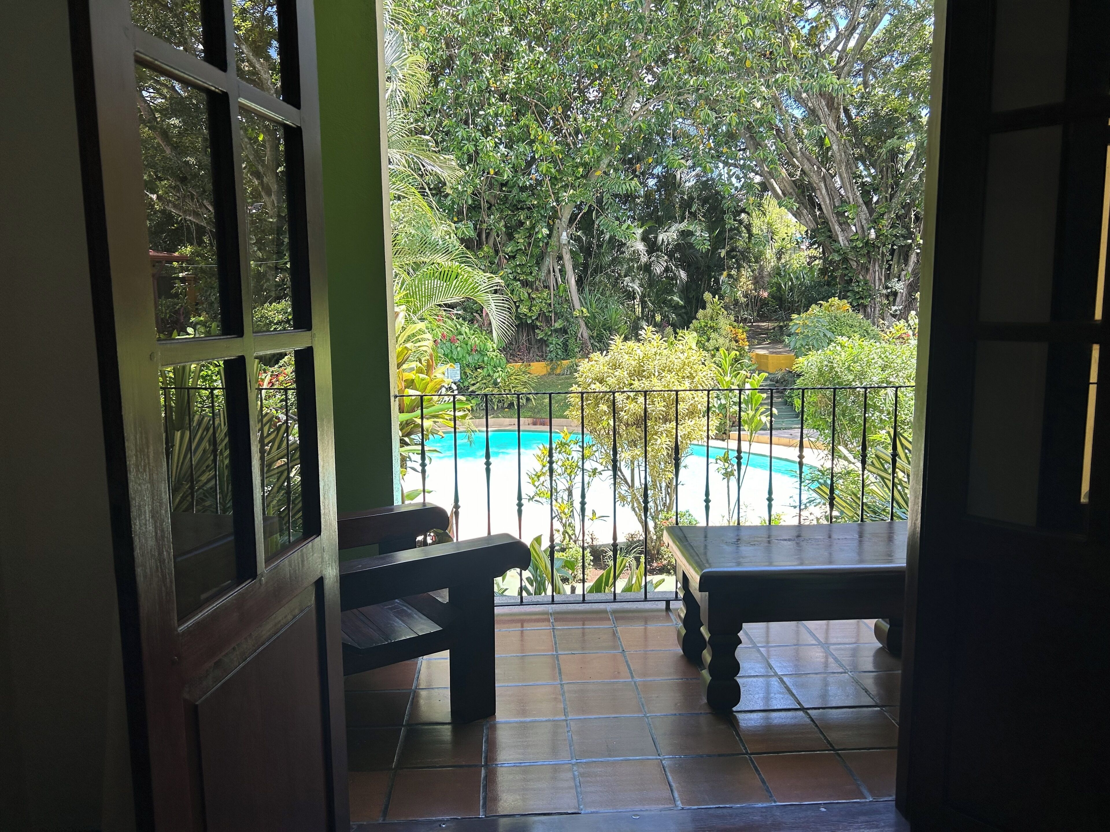 Une vue depuis un balcon donnant sur une piscine, le tout entouré d’une végétation luxuriante.