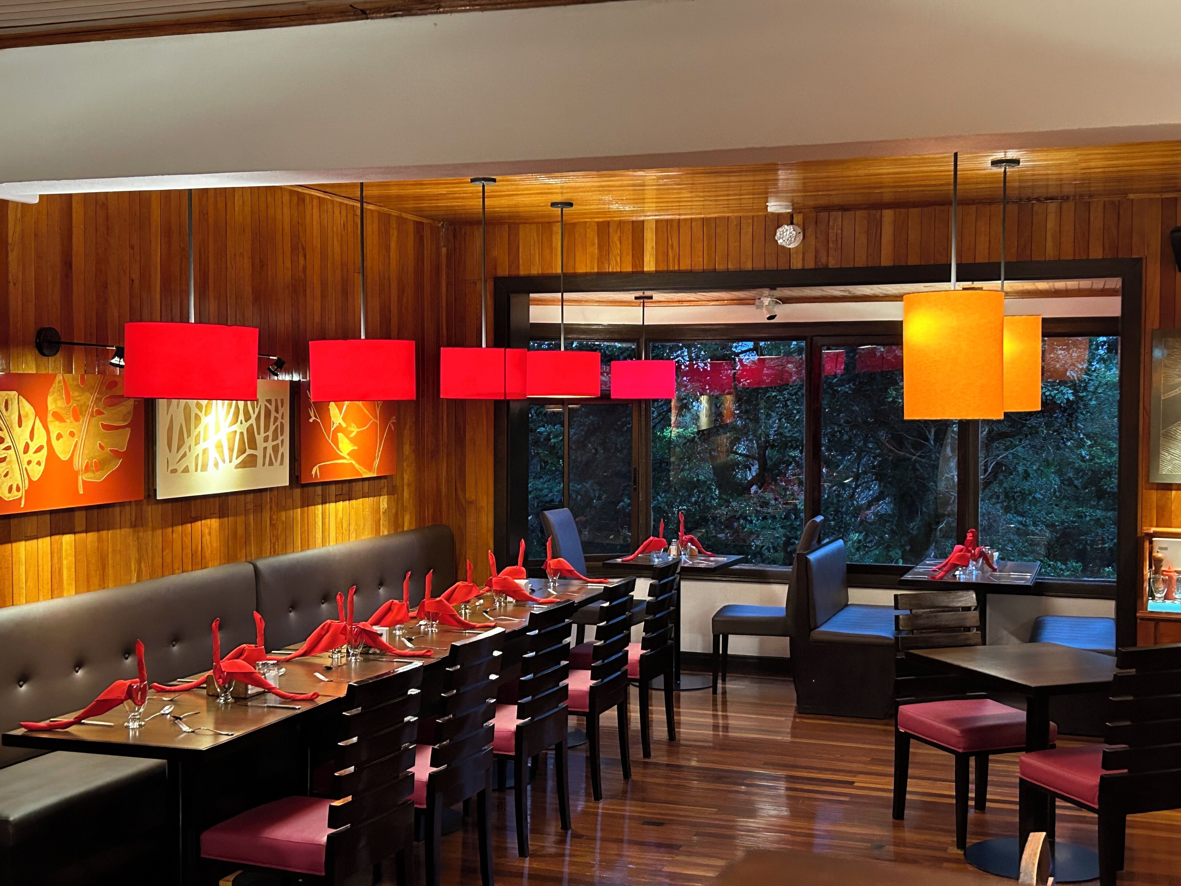 Un restaurant doté d’un long banc en bois servant de banquette, de tables décorées en rouge et d’un éclairage suspendu.