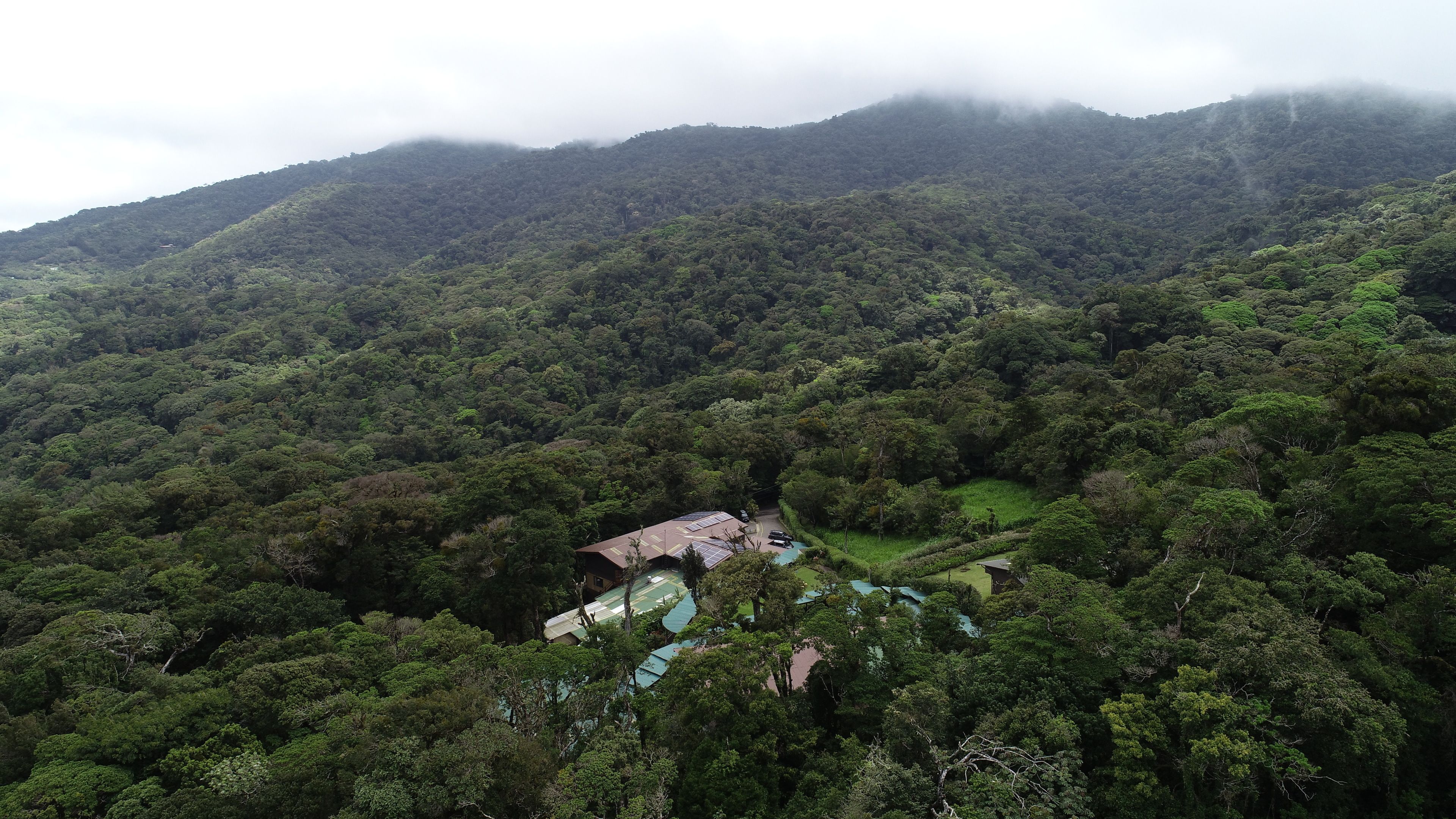 A mountainous landscape with dense forest. A small building with solar panels is visible.