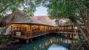 Un restaurant situé au bord de la rivière, doté d’une terrasse en bois et de structures à toits de chaume.