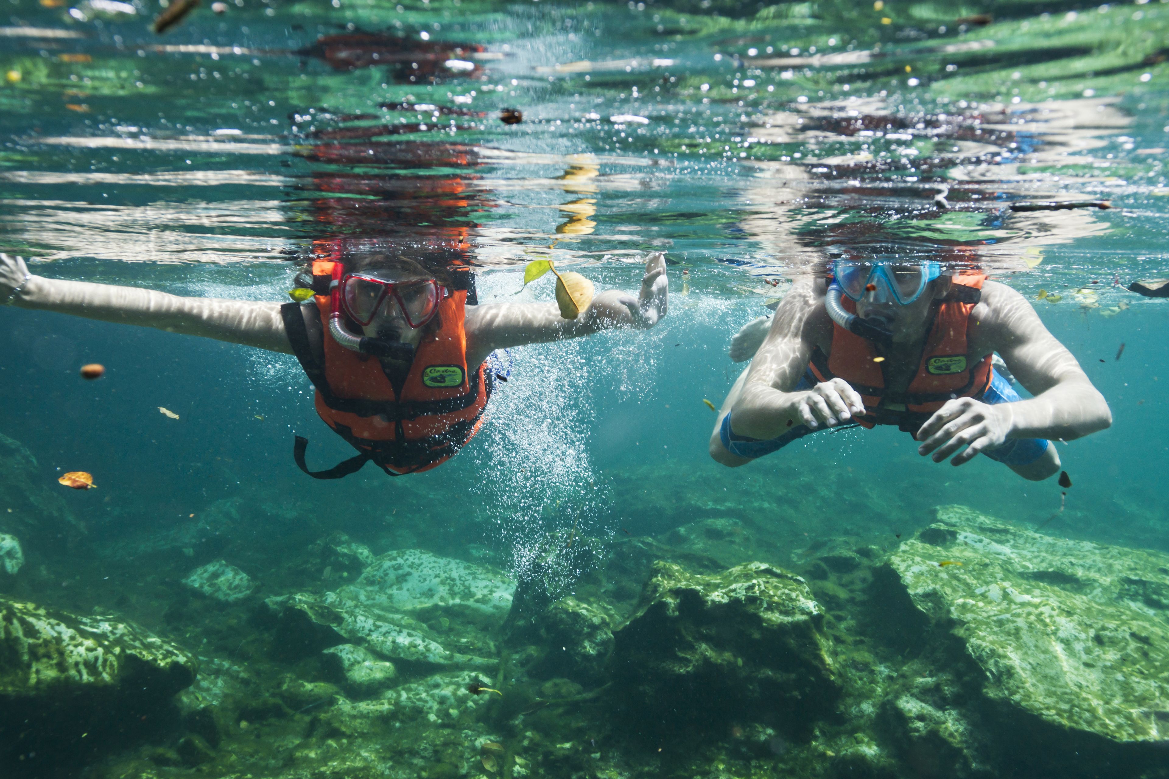 Two people snorkeling underwater with clear water and rocks.