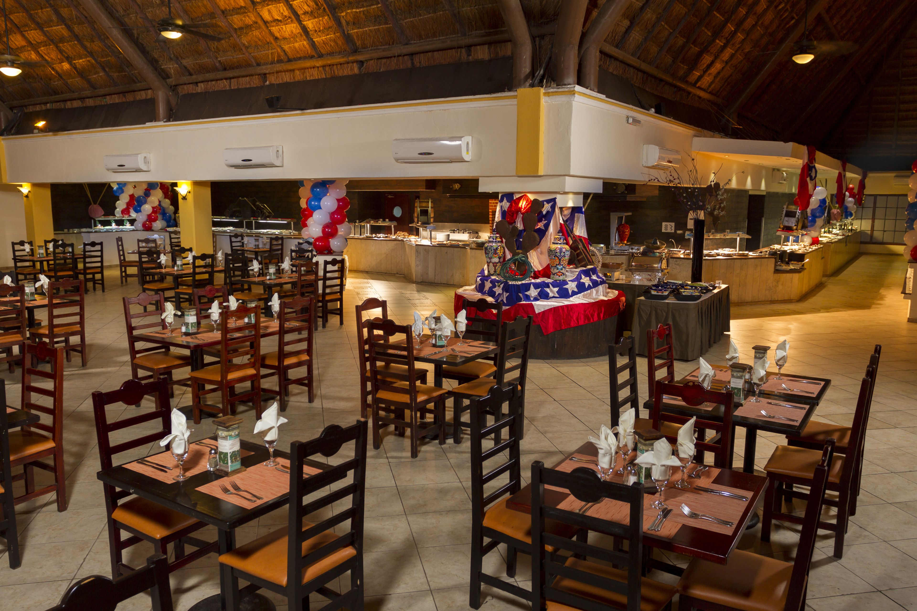 A spacious dining area with multiple tables and chairs, air conditioning units, and a buffet setup.