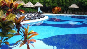 A swimming pool with lounge chairs and thatched umbrellas, surrounded by lush greenery. -  Select Club at Sandos Caracol All Inclusive - Adults Only Area (Playa del Carmen)