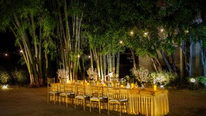 An outdoor dining area with a long table set for guests, surrounded by bamboo trees and illuminated by string lights. - Country Inn Tarika Resort Jim Corbett (Ramnagar)