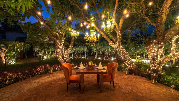 An outdoor dining area with a table set for two, surrounded by trees adorned with string lights. - Country Inn Tarika Resort Jim Corbett (Ramnagar)