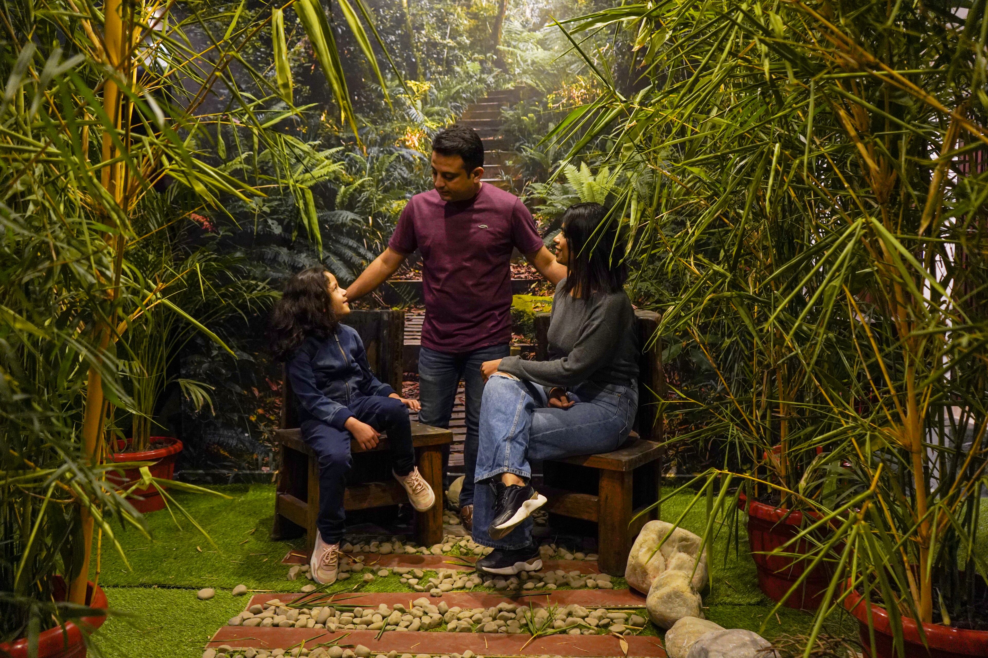 A group of people sitting on wooden benches in a lush indoor garden with various plants and a small waterfall feature.