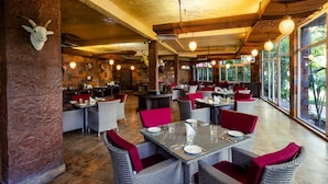 A restaurant with high tables and chairs, a stone wall with a mounted animal head, and large windows offering a view of the outdoors. - Country Inn Tarika Resort Jim Corbett (Ramnagar)