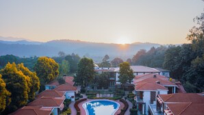 A resort with a swimming pool surrounded by buildings with red-tiled roofs, set against a backdrop of mountains and trees. - Country Inn Tarika Resort Jim Corbett (Ramnagar)