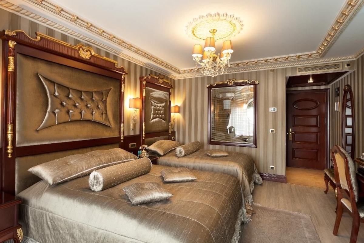 A luxurious hotel room with a large bed, two bedside tables, a chandelier, and a mirror.