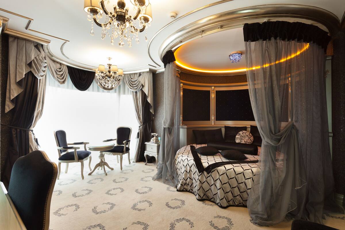 A luxurious bedroom with a large bed, a chandelier, and a view of the city.
