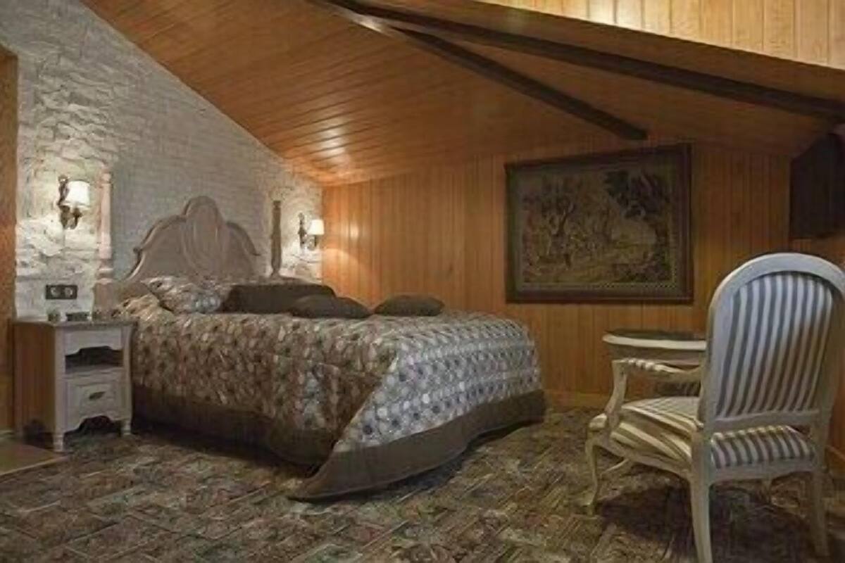 A bedroom with a bed, a chair, a nightstand, and a painting on the wall.