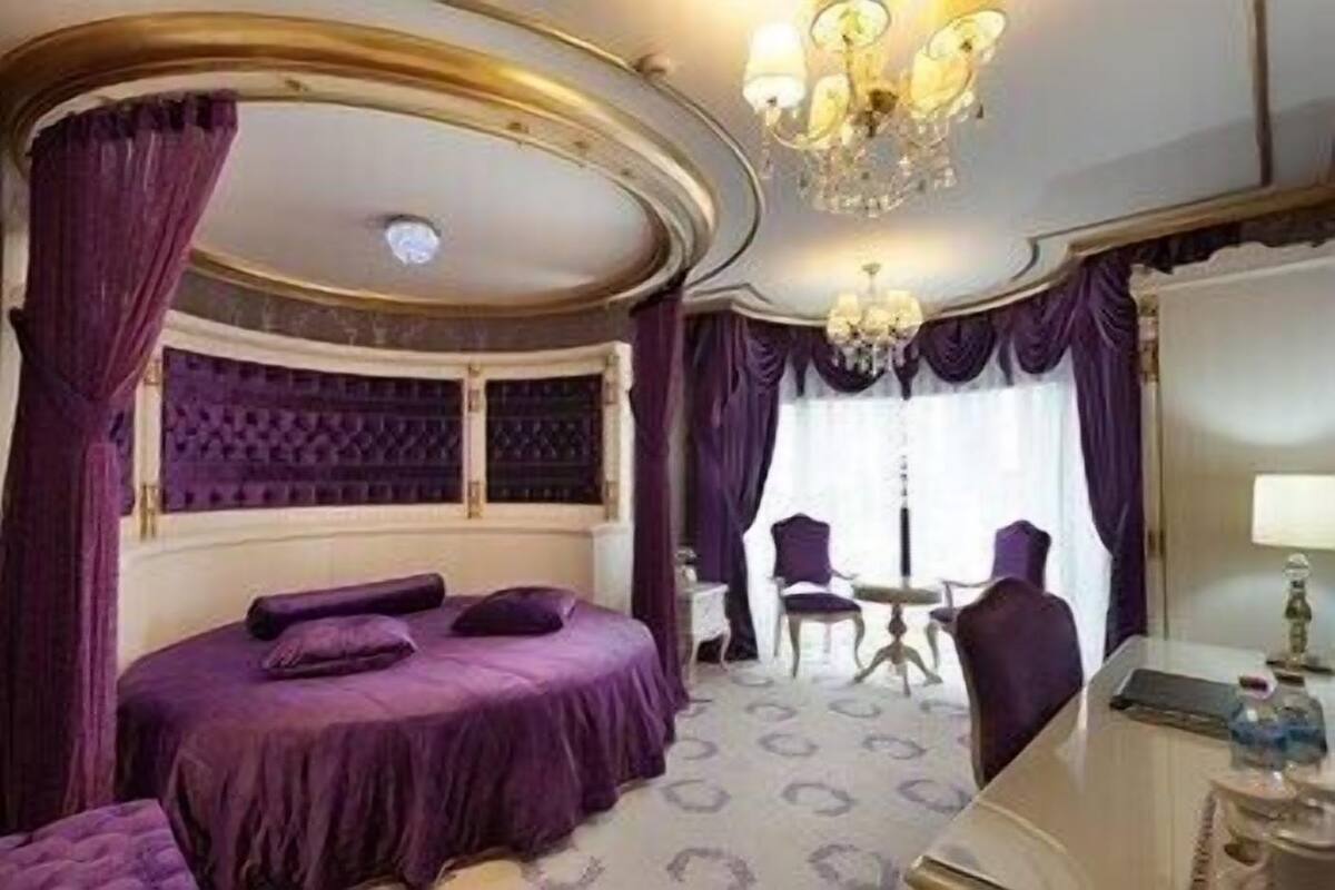 A room with a bed, a chandelier, a desk, and a chair.