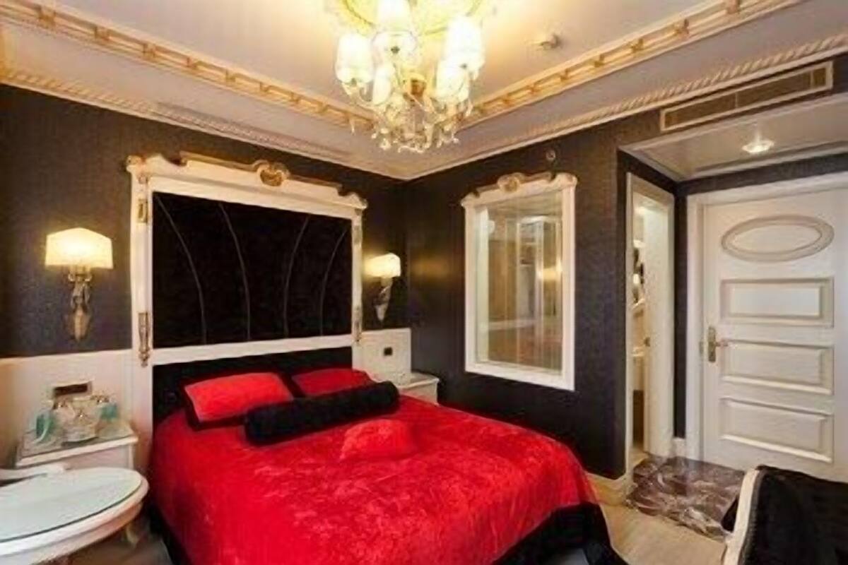 A bedroom with a large bed, a chandelier, a mirror, and a door.