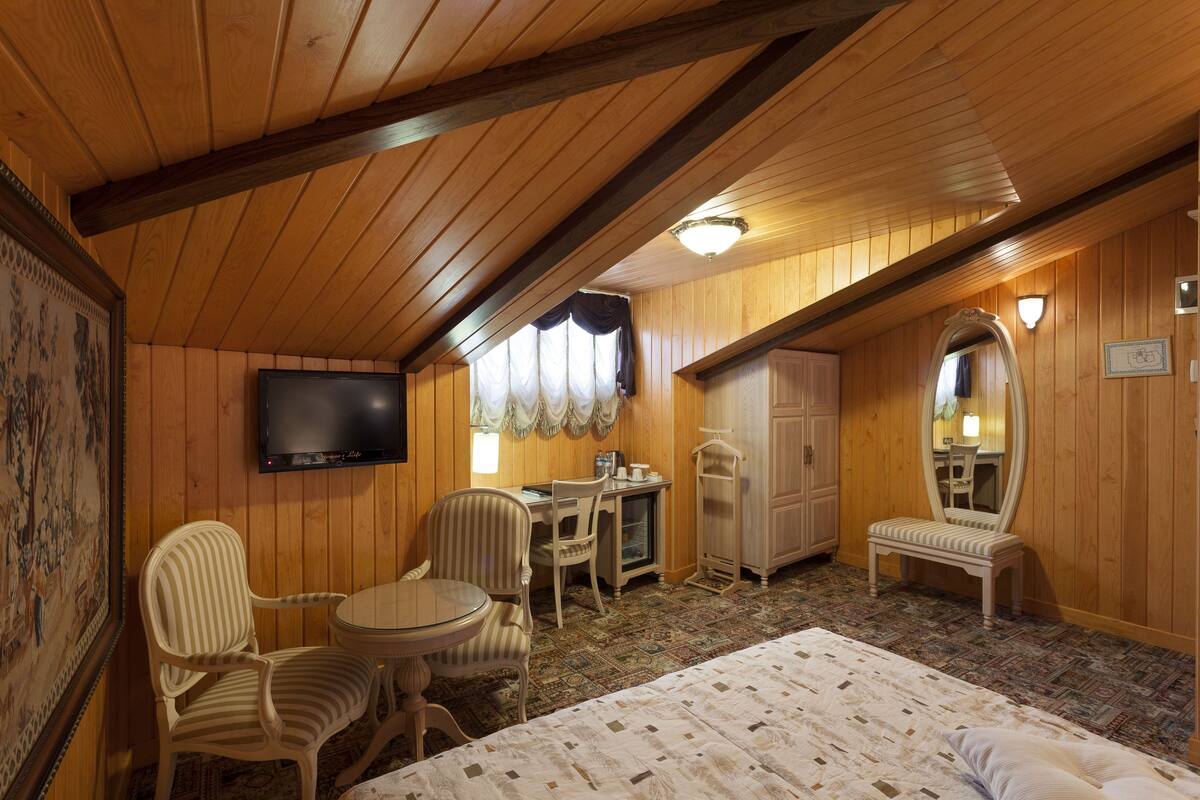 A cozy room with a bed, a desk with a chair, a television, and a mirror.