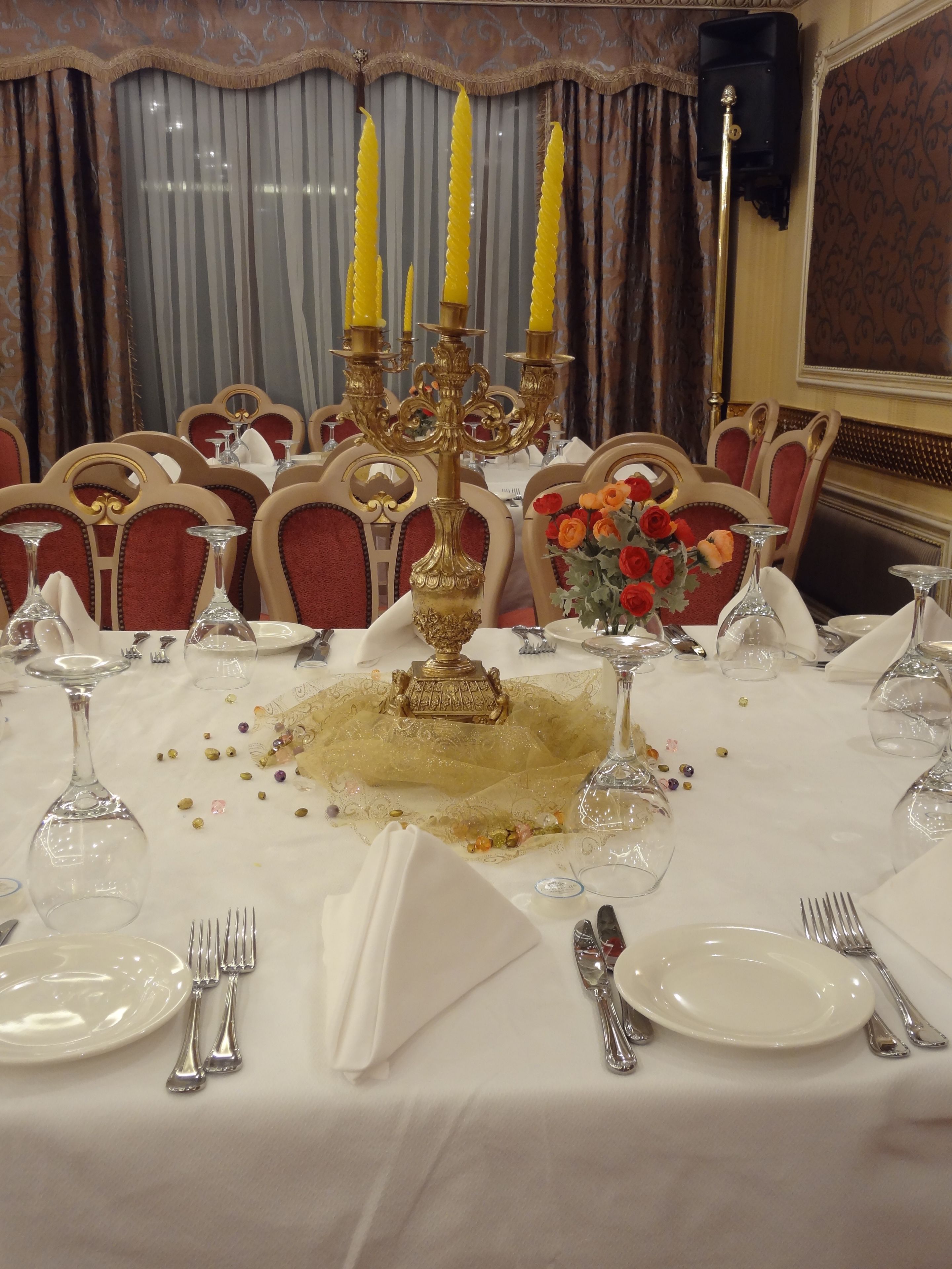 A formal dining table set with white tablecloth, gold candelabra, and red chairs.
