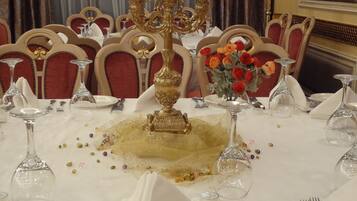 A formal dining table set with white tablecloth, gold candelabra, and red chairs.