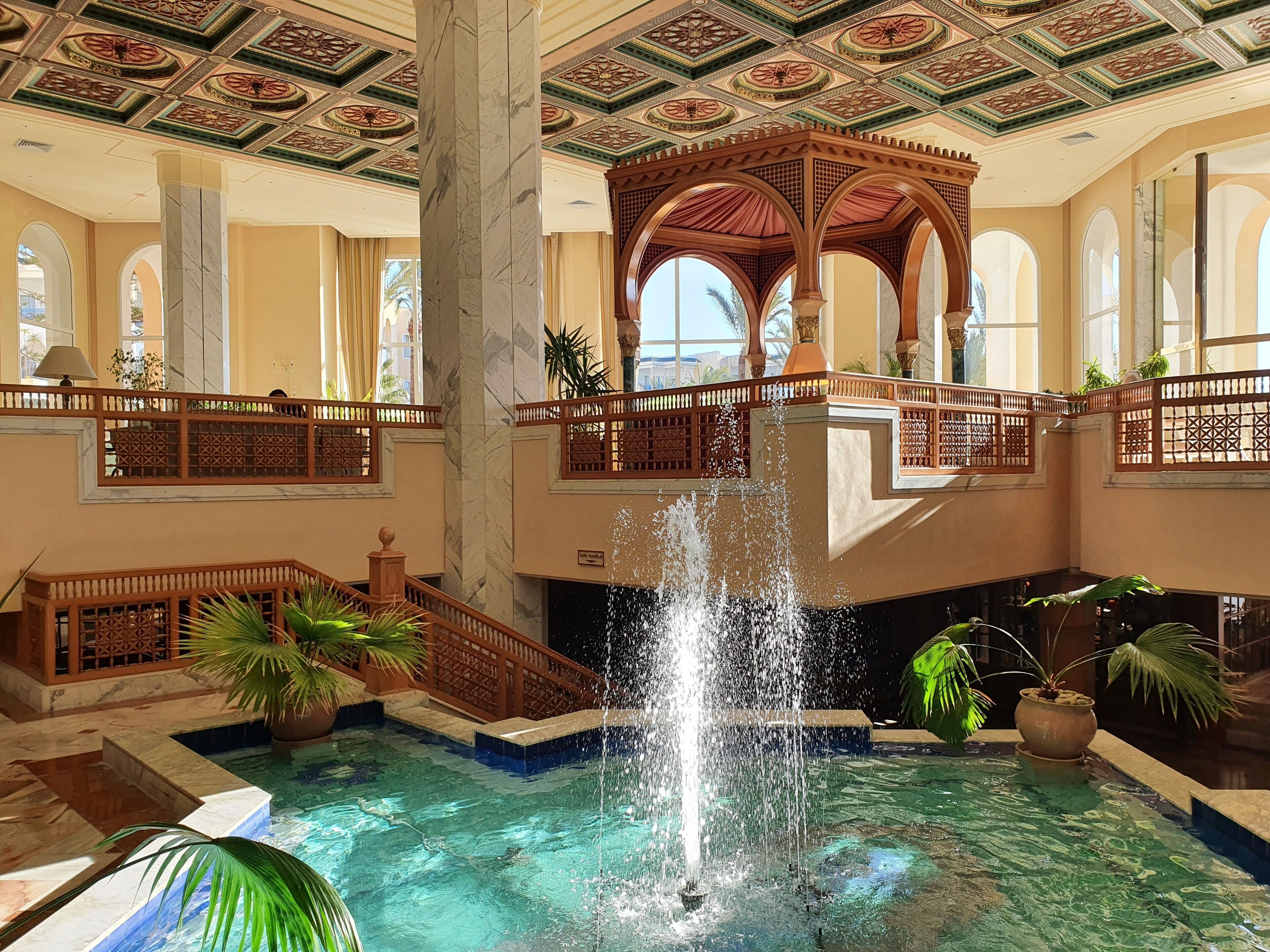 Ein luxuriöser Innenpoolbereich mit einer zentralen Fontäne, einer verzierten Decke und einem Balkon mit Blick auf den Pool.